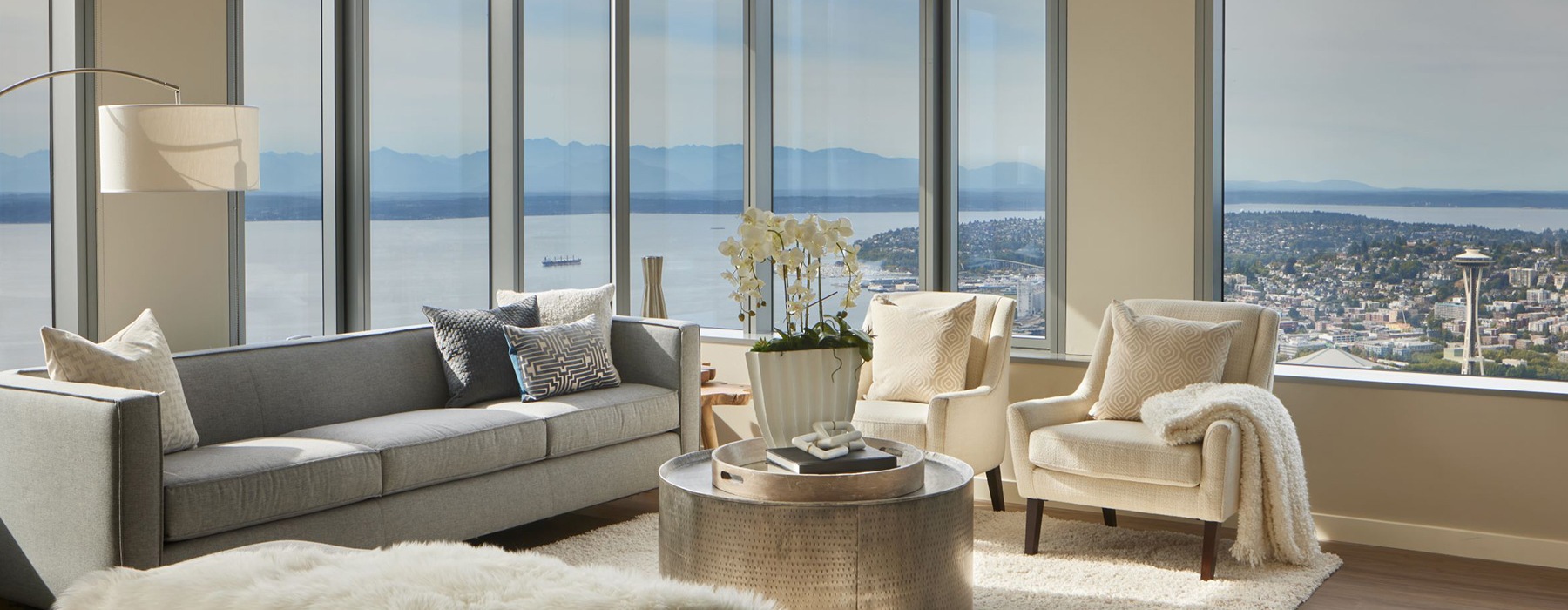 spacious living room with modern furniture and ample lighting from wall-to-corner windows also showing wide city views